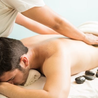 Closeup of a female therapist giving a hot stone massage to a young man in a spa